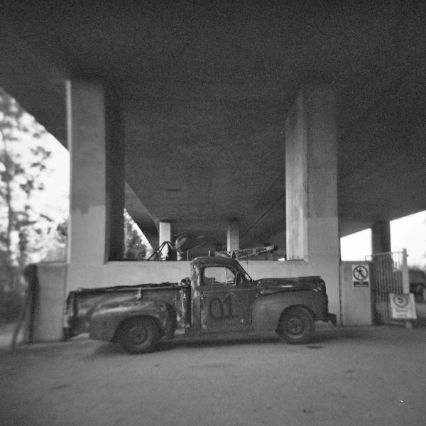 Black and white photo of an old American pickup truck beneath a concrete flyover