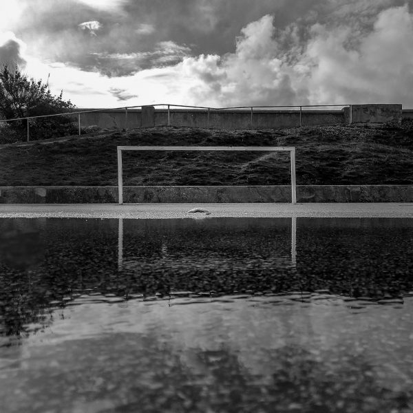 Black and white photo iftan empty goal reflected in a large puddle