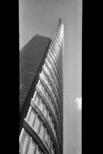 Vertical panoramic photograph, in black and white, of a curved, metallic skyscraper in London