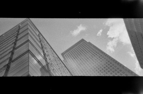 Grainy panoramic black and white photo looking up at city high-rise skyscrapers with clouds behind