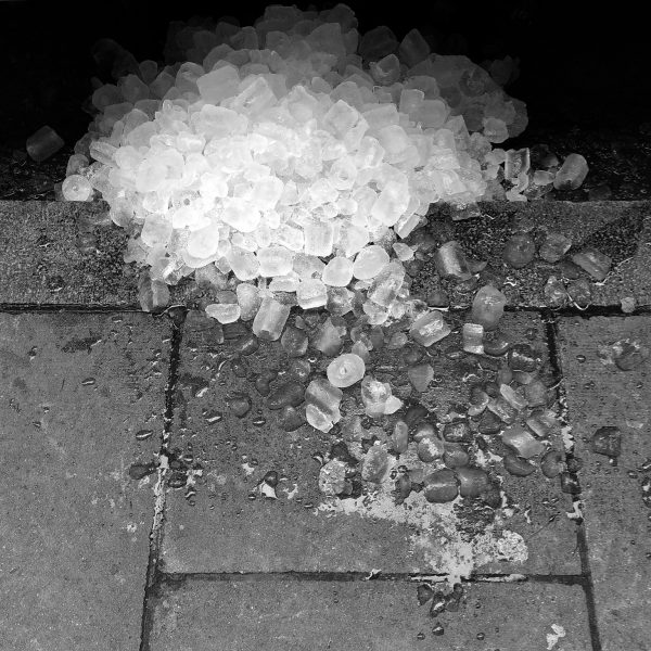 A huge pile of ice cubes, scattered over the edge of a pavement.