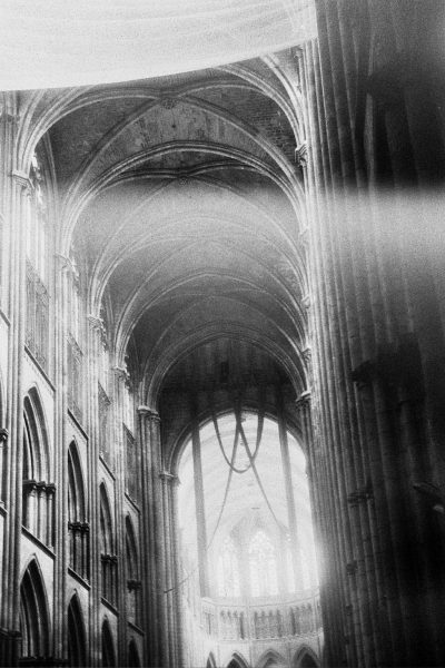 The inside of a large church or cathedral, with high arches shadowed against bursts of incoming light.