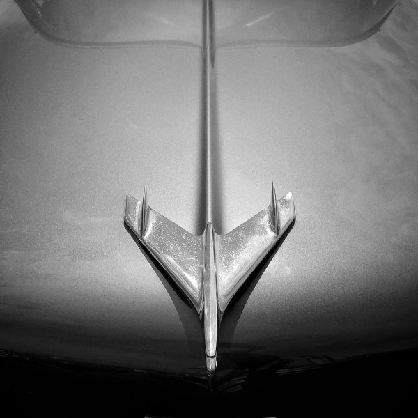 Black and white photo of a stylish aeroplane model mounted on the curved bonnet of a car