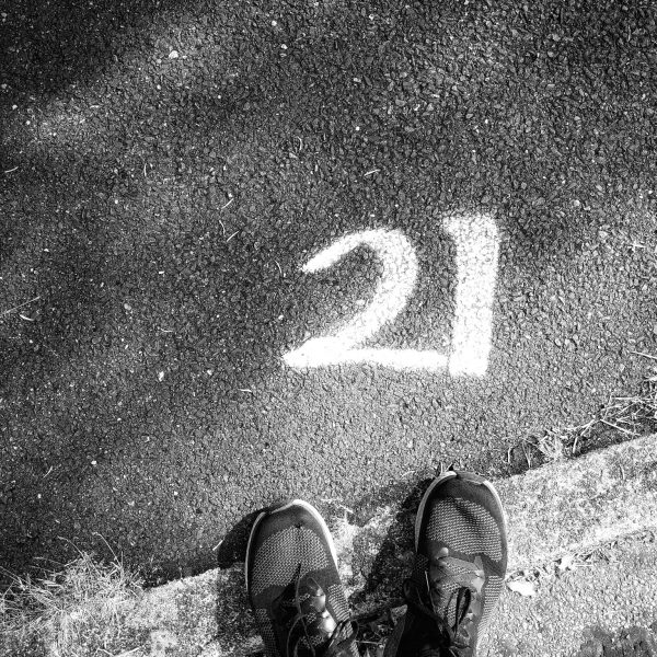 Black and white photo looking down at my shoes, with a large white number 21 painted on the pavement in front of them