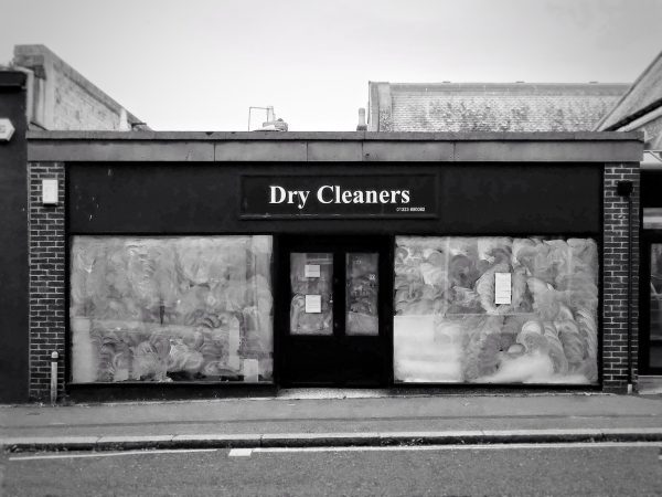 Black and white photo of a dry cleaners store, its windows covered in swirls of white paint